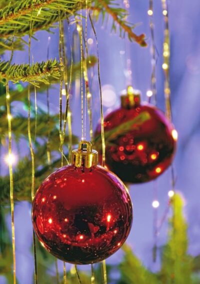Red Christmas ornaments hang from a tree, surrounded by golden strands and soft, glowing lights in a festive setting