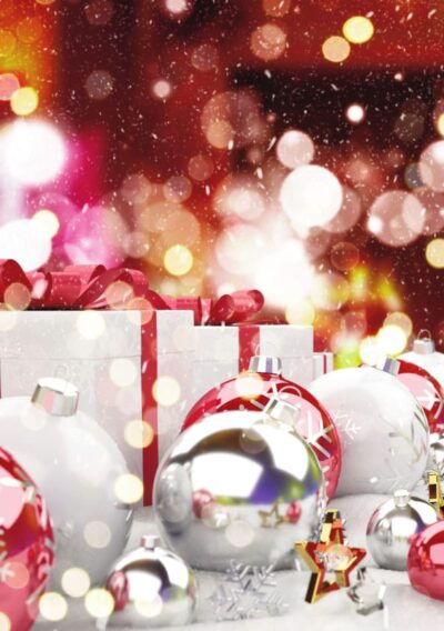 Colorful Christmas ornaments and wrapped gifts are scattered on a snowy surface, with a festive bokeh background