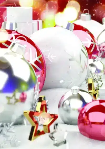 Colorful Christmas ornaments, including red and white balls with snowflake designs, scattered on a snowy surface with gifts
