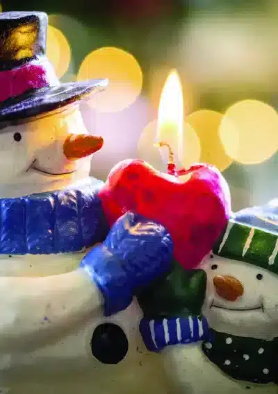 Two cheerful snowmen hold a red heart candle, glowing warmly against a blurred festive background. Snowmen and the Red Candle