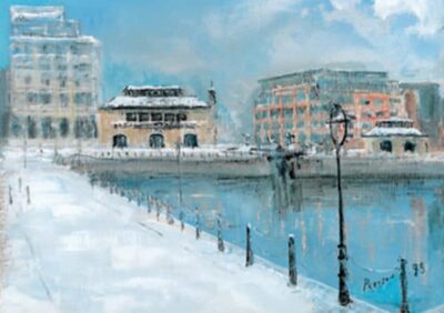 Snow-covered waterfront scene featuring buildings, a lamppost, and a calm river under a blue sky